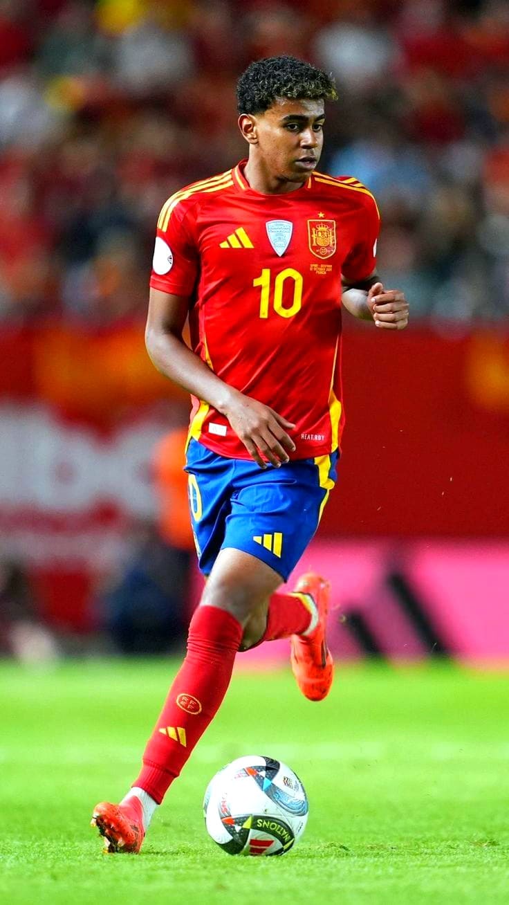 A male soccer player in a red and yellow Spain jersey with number 10 dribbles a ball on a field during a match, as fans watch from the blurred background stands—perfect action for viewers catching the excitement via IPTV Italy.