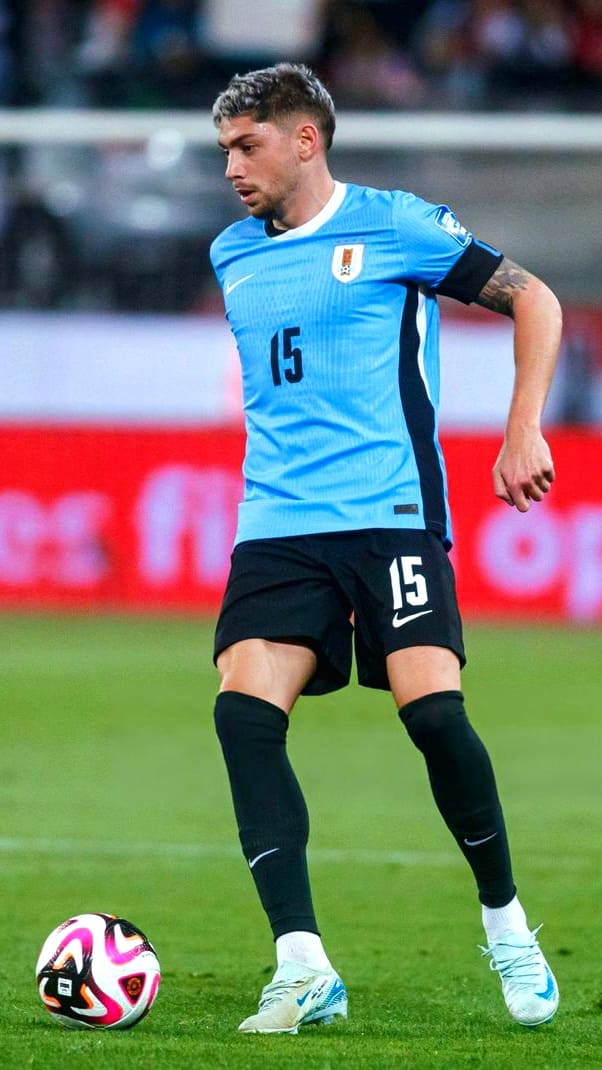 A soccer player in a light blue jersey with the number 15 controls a ball during a match on a grass field. He has short hair and wears black shorts, black socks, and white shoes. For fans watching from afar, services like IPTV Italy bring exciting moments like these directly to your screen.