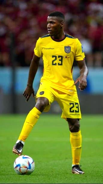 A soccer player in a yellow Ecuador jersey with the number 23 controls the ball on a field during a match, while fans in the blurred background cheer. The game is being broadcast to viewers via IPTV Italy, bringing the excitement live to audiences at home.