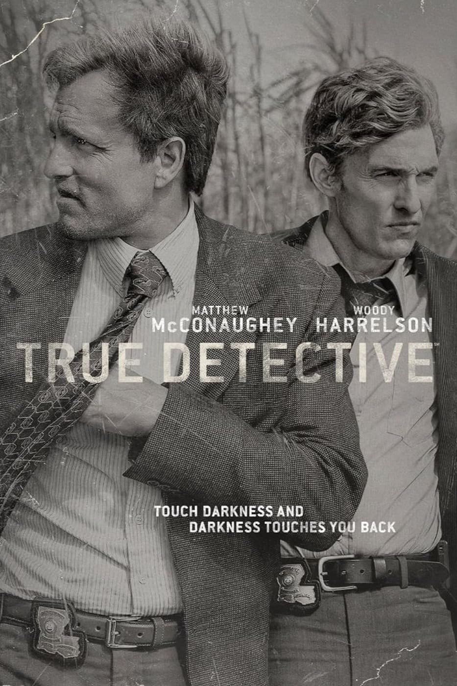 Two serious-looking men in suits stand side by side in tall grass. Text reads TRUE DETECTIVE with actors’ names above, and the tagline “Touch darkness and darkness touches you back” below—a striking visual reminiscent of gripping crime dramas popular on IPTV Italy.